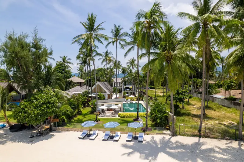 Mandarin Beach Villa seen from the beach, with the pool, lawn and Thai pavilions behind tall palms.