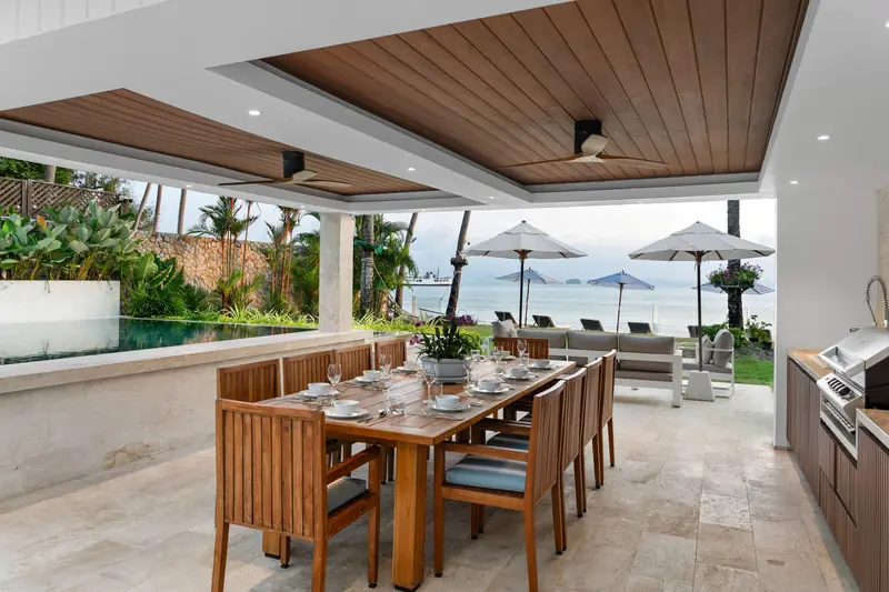 Outdoor dining table set beneath the beachfront pavilion with loungers and the sea beyond.