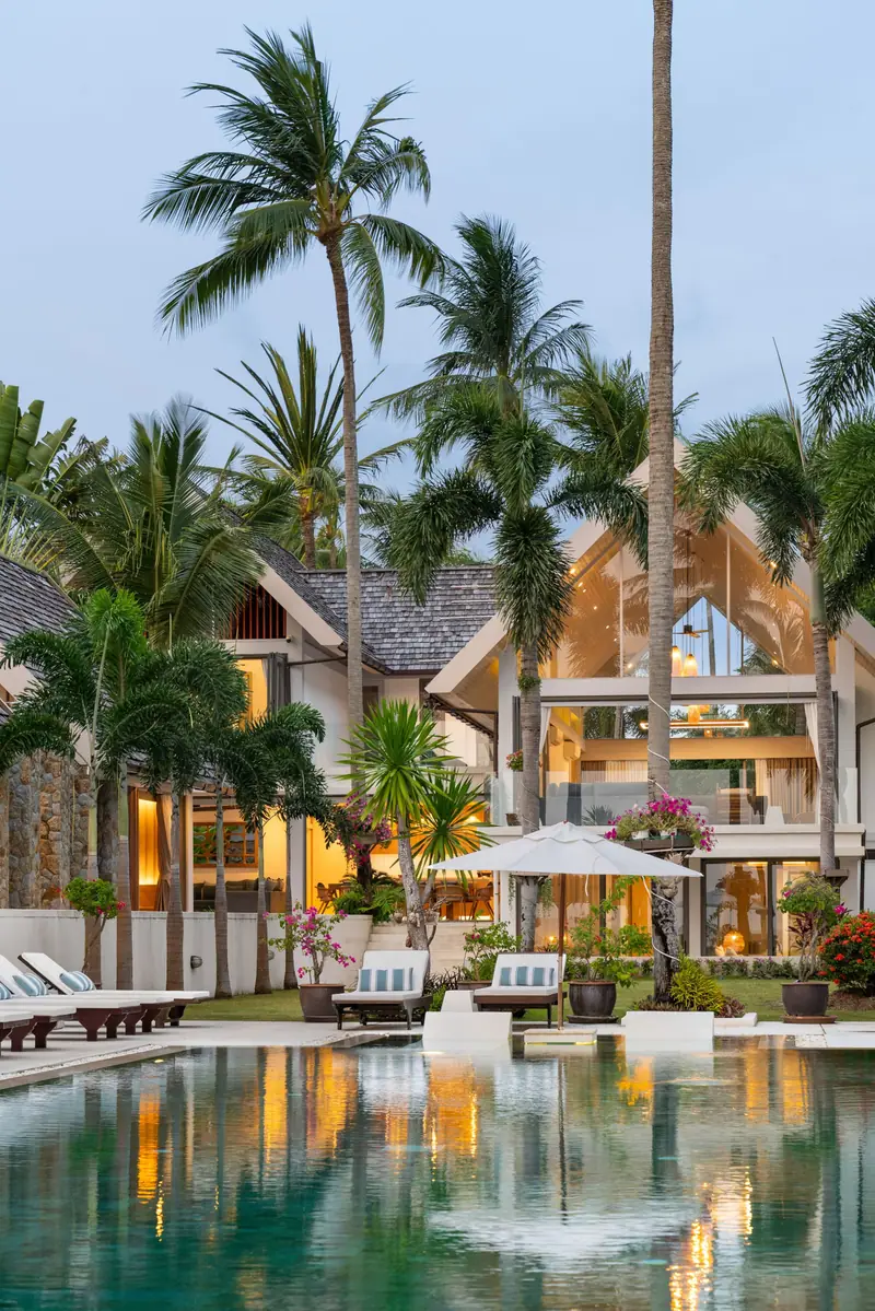 Portrait of the timber-and-white Thai pavilion architecture framed by palm trunks and foliage.