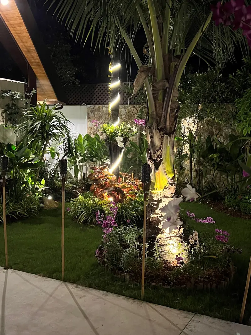 A shaded tropical garden corner with lush leaves, flowers and a decorative figure.