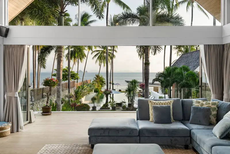 Grey sofa in a lounge opening onto palms and the sea.
