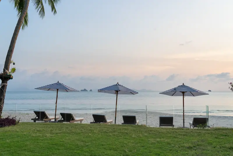 Loungers and umbrellas on the sand at sunset with the sea beyond.