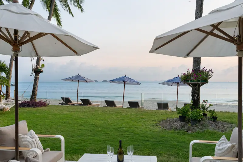 Umbrellas and loungers on the sand in front of the lawn, with the sea beyond.