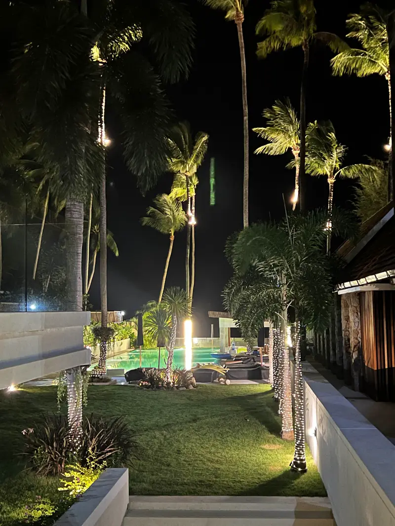 Palms and the pool pavilion lit at night.