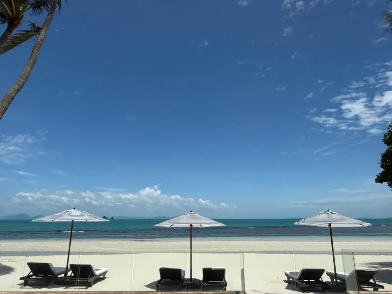 Umbrellas and loungers on white sand with the sea beyond.