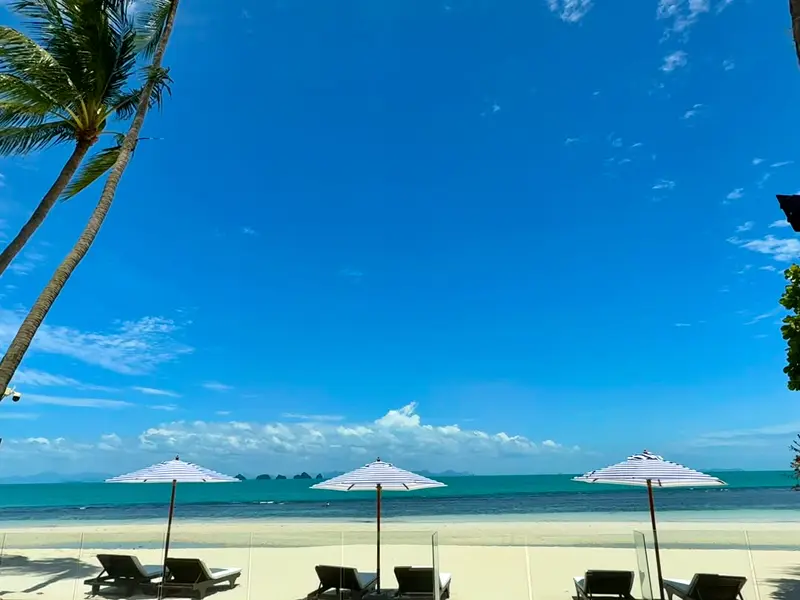 Three striped umbrellas on the white sand with the turquoise sea, the islands and a blue sky beyond.