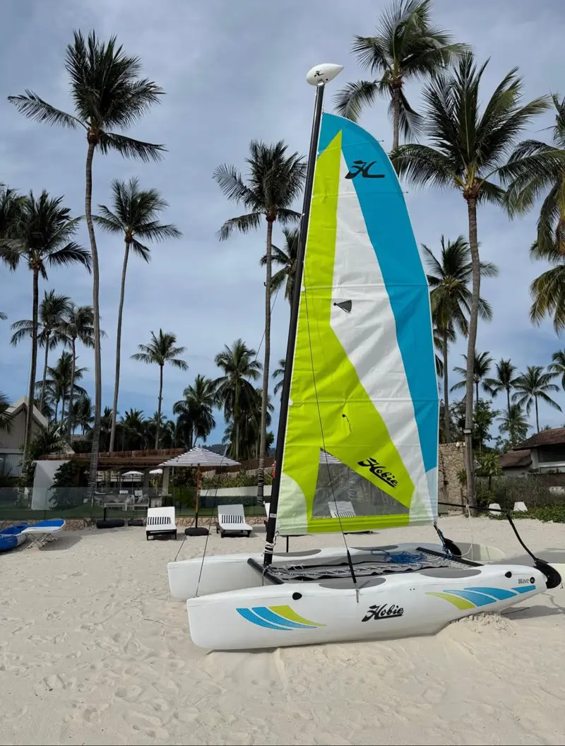Mandarin Beach Villa’s Hobie Cat catamaran, rigged with its lime and blue sail, on the sand in front of the villa.