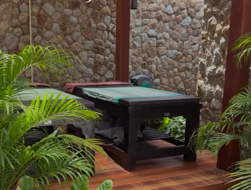 Two massage beds on a timber deck in Mandarin Beach Villa’s open-sided sala, with a stone wall behind and palms around.