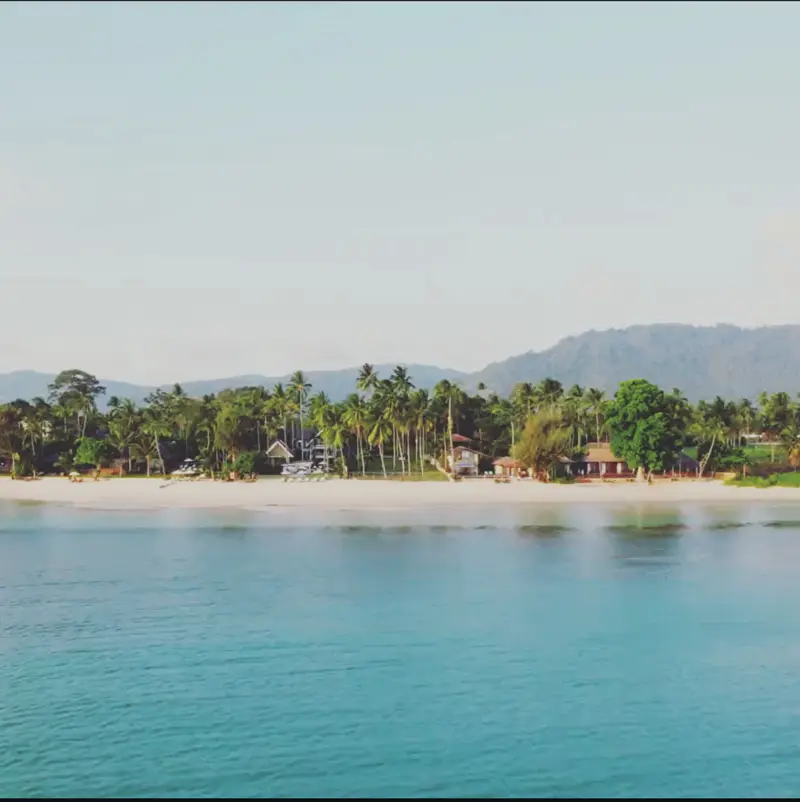 A long stretch of Lipa Noi beach seen from the sea, with palms and hills behind.
