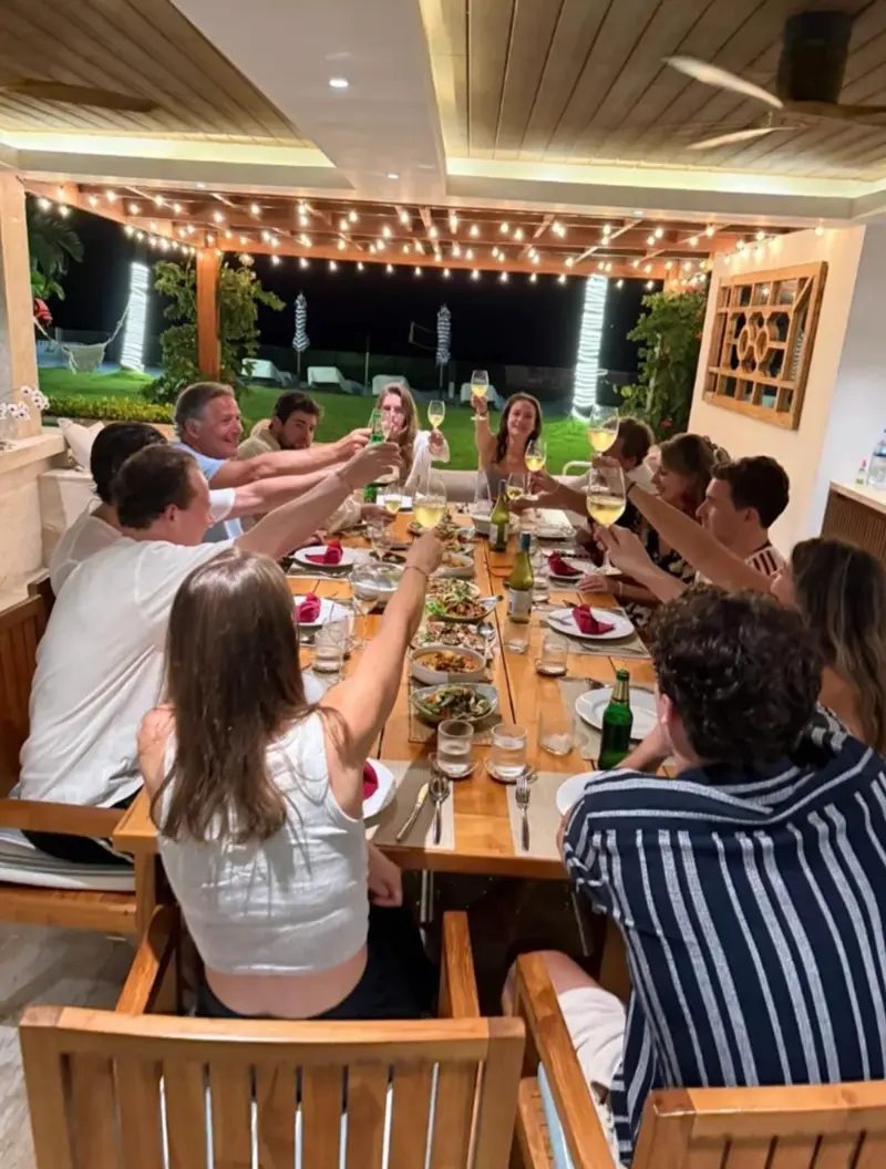 Guests at Mandarin Beach Villa raising their glasses at a long dinner table under strings of lights in the garden pavilion at night.